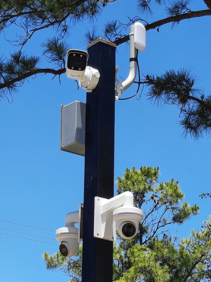 A pole with several cameras on it and trees in the background.