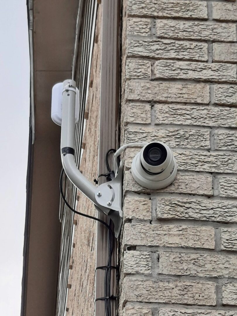 A white security camera mounted to the side of a brick building.