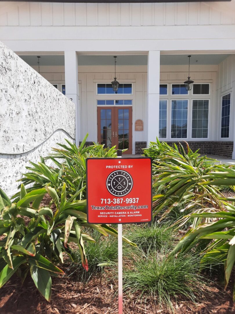 A red sign in front of a house with bushes.