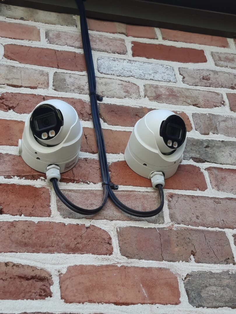Two white security cameras mounted on a brick wall.